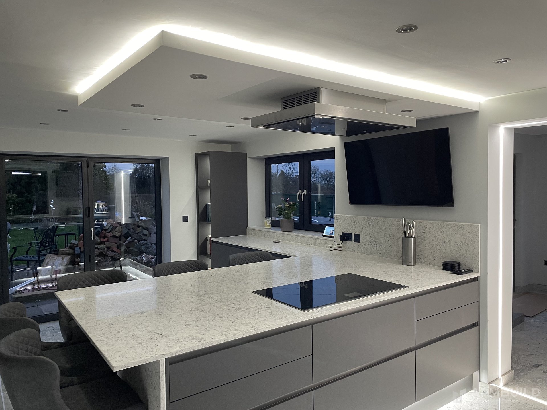 Completed open-plan kitchen with quartz island, statement hood, and LED-cove ceiling in a Gorsley home by APMBuild, Herefordshire
