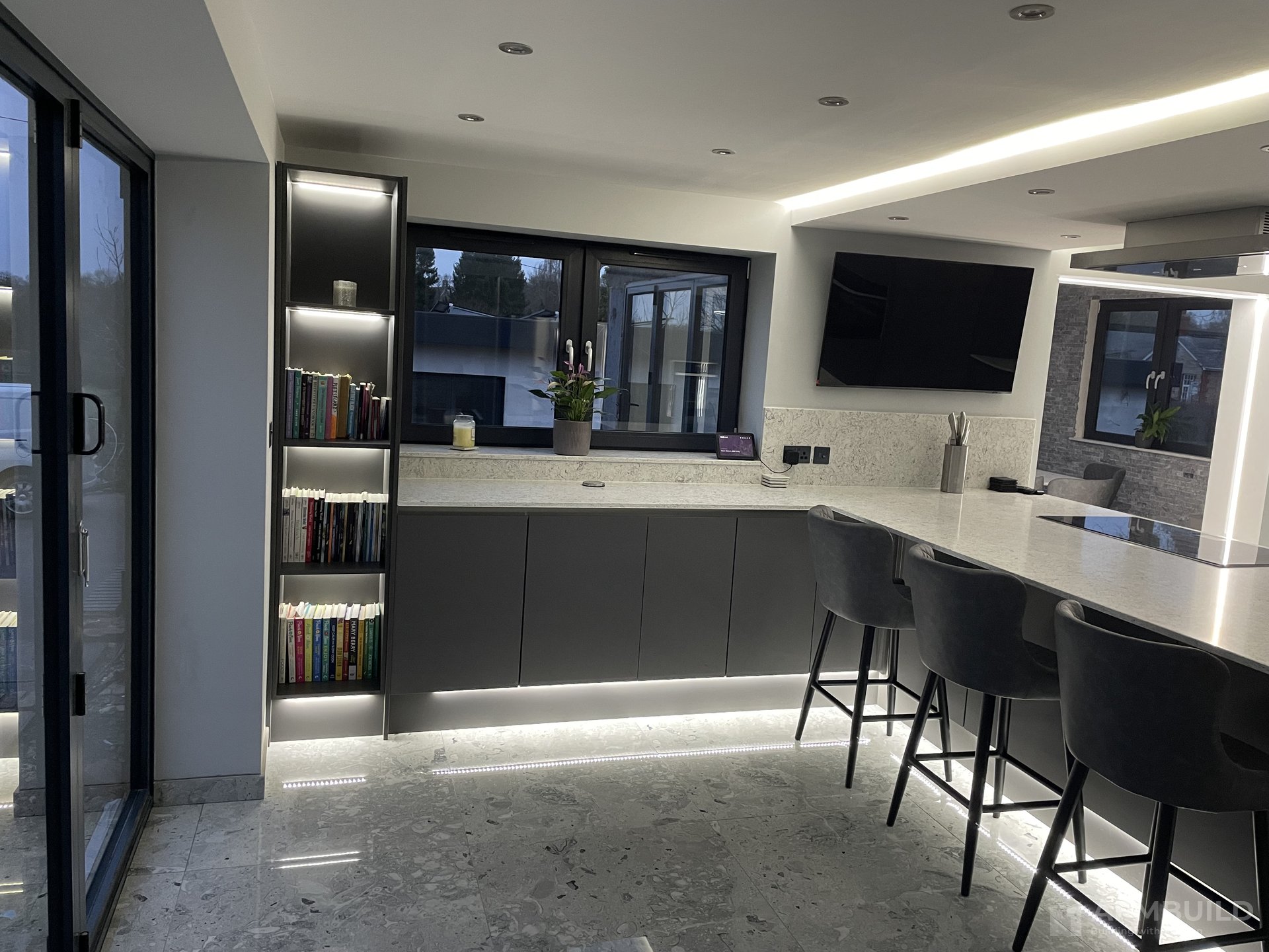 Finished Gorsley kitchen with backlit book wall, grey cabinetry and breakfast bar by APMBuild, Herefordshire