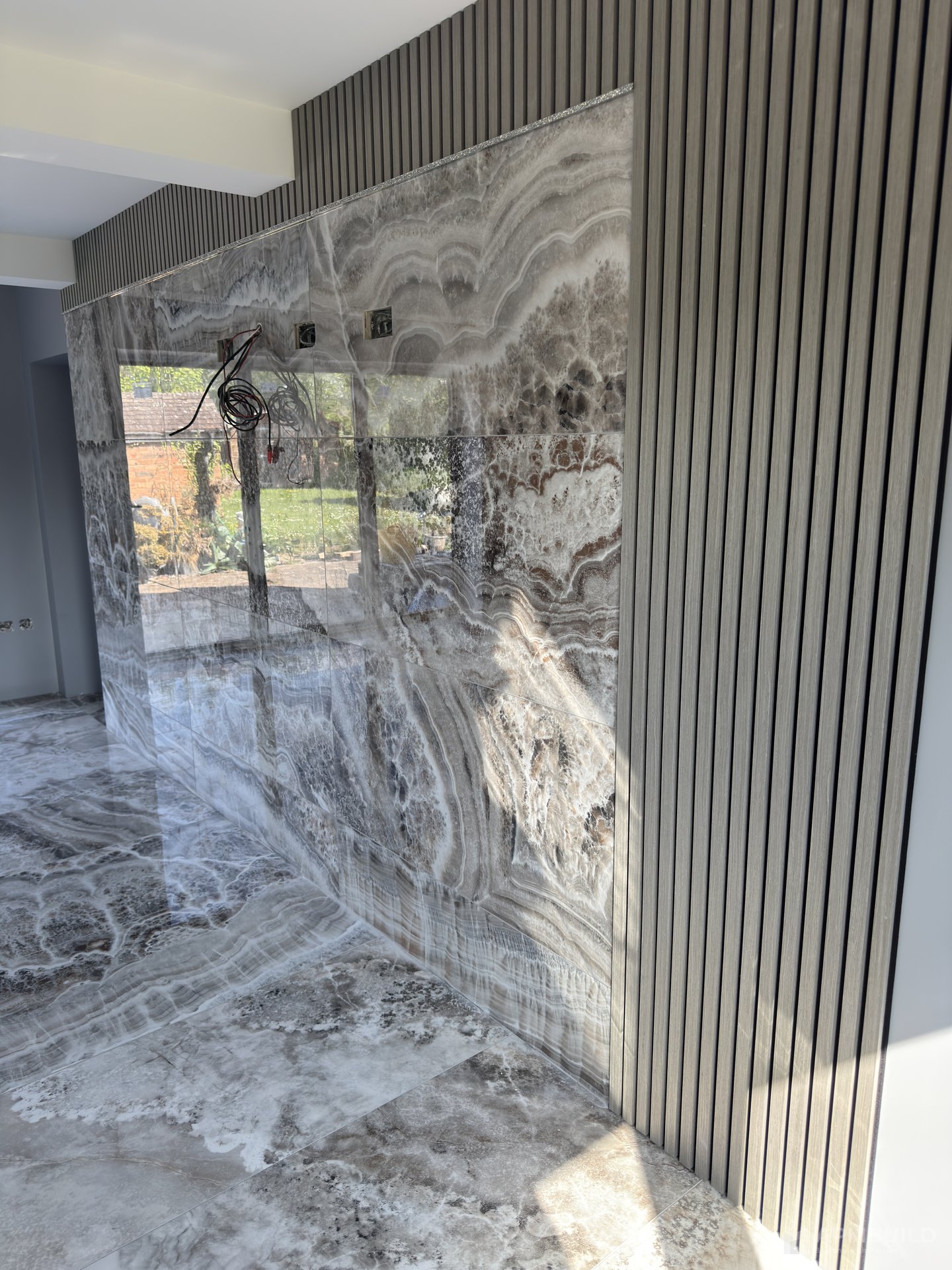 Polished onyx slab feature wall framed by slatted oak panels in a Gorsley home by APMBuild, Herefordshire