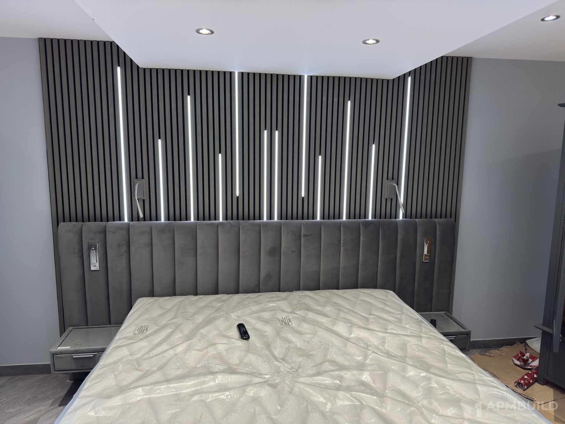 Finished Gorsley master bedroom with backlit slatted panel wall and upholstered headboard by APMBuild, Herefordshire