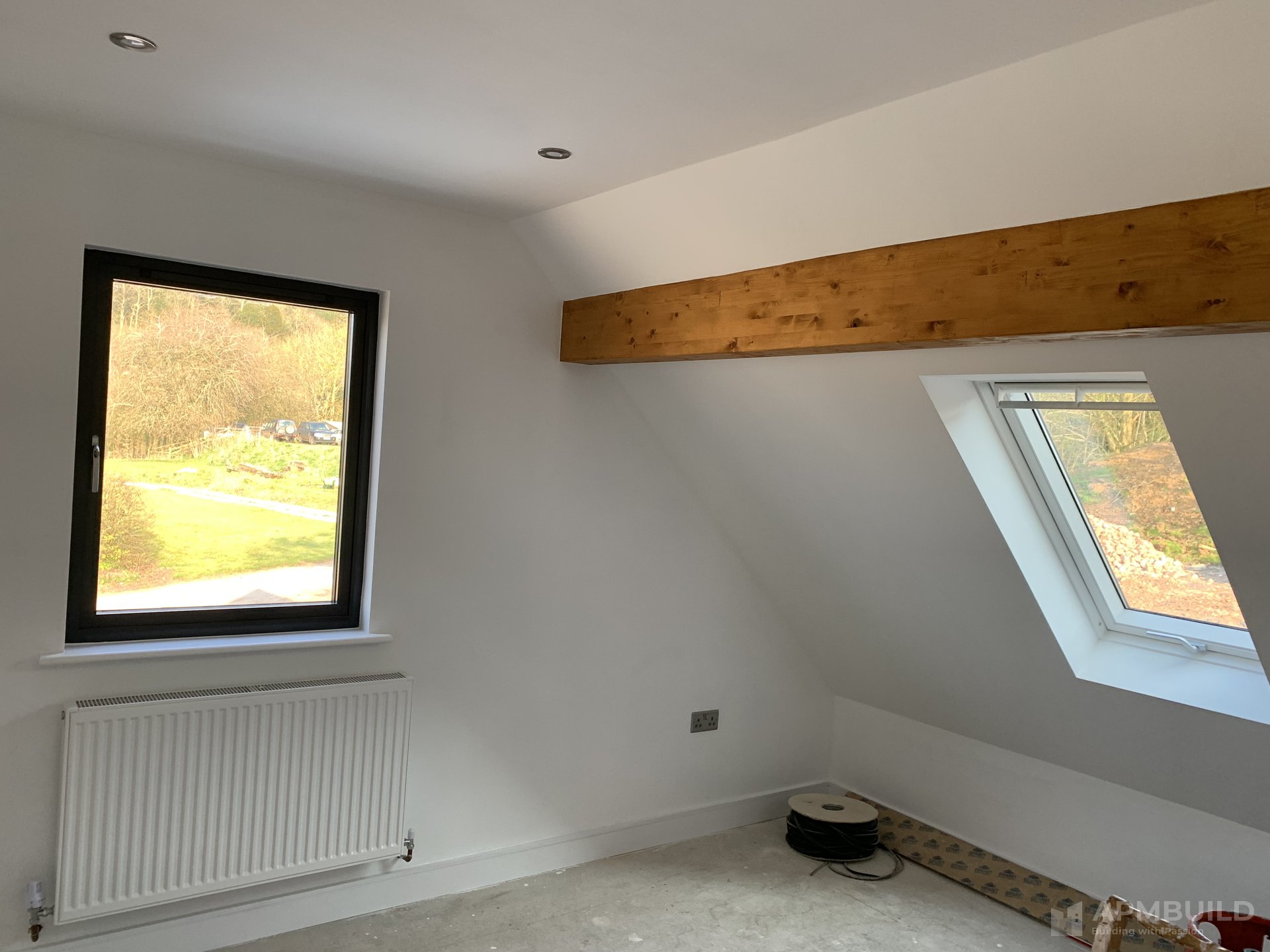 Completed loft bedroom with exposed timber beam, anthracite window and Velux rooflight in Hole in the Wall Ross-on-Wye by APMBuild