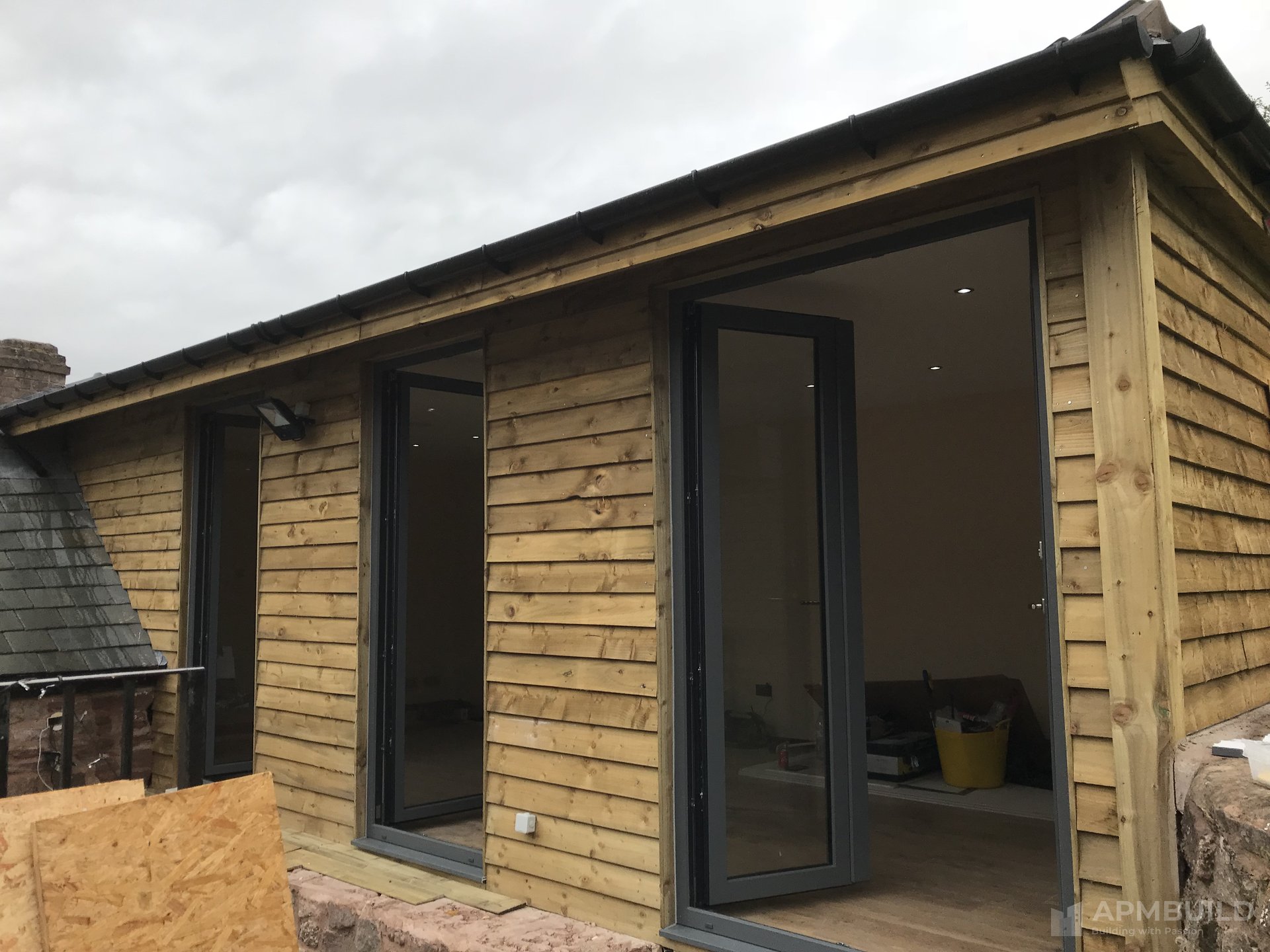 Completed timber-clad garden gym building with bi-fold doors and slate trim in Lea Ross-on-Wye by APMBuild, Herefordshire