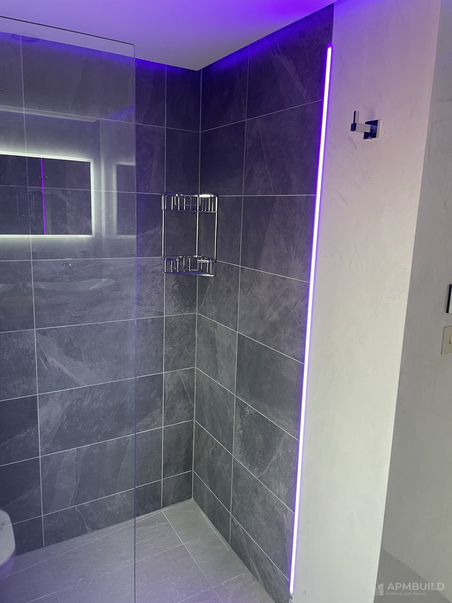 Bathroom with microcement walls, dark porcelain tile and chrome thermostatic shower in Saxon Gate Hereford by APMBuild