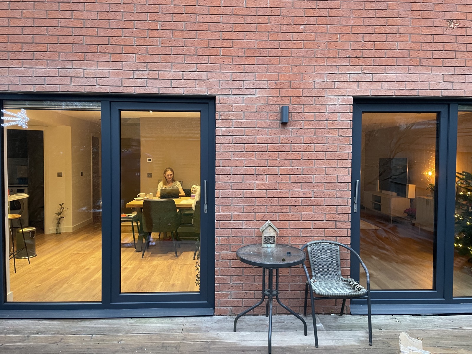 Saxon Gate rear elevation after APMBuild rebuild — two large dark aluminium sliding patio doors framing a central brick pier with security light, opening onto a timber deck
