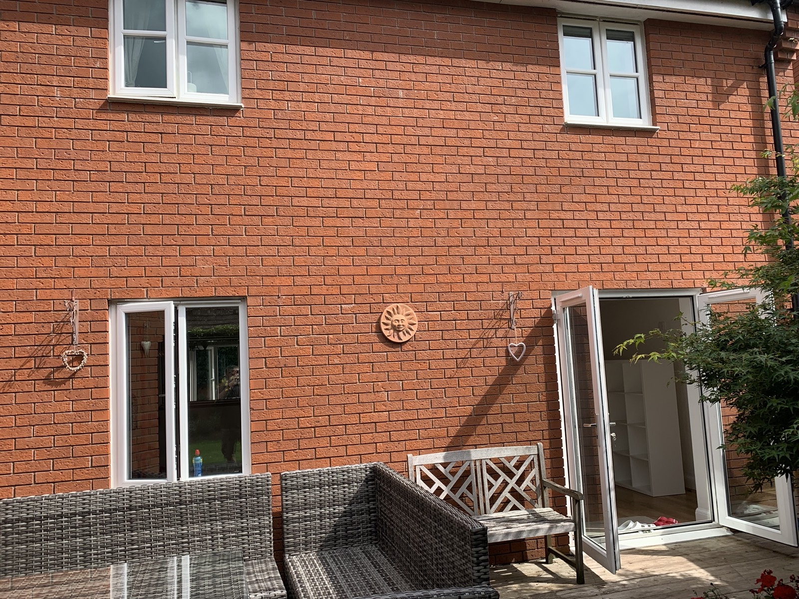 Saxon Gate rear elevation before APMBuild rebuild — original brick wall with a single small uPVC casement window and narrow uPVC door, decorative hanging hearts and patio furniture